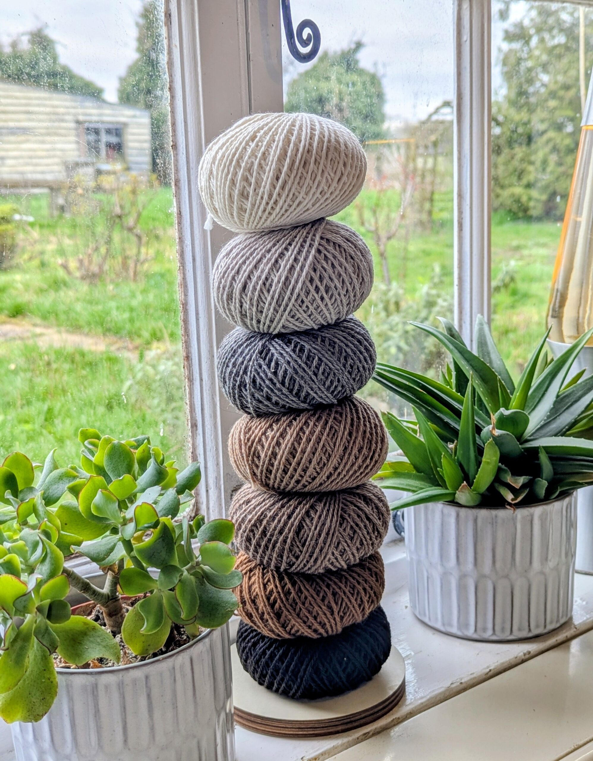 stack of 50g balls of alpaca yarn in window with plants either side