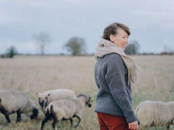 woman wearing dark grey jumper standing in front of a flock of sheep