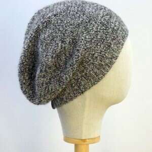 side view of a black and white mottled slouchy beanie displayed on a white display head