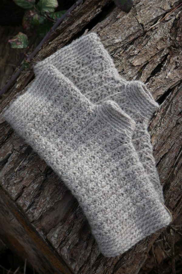 light grey crochet wrist warmers on a wooden log. textured design.