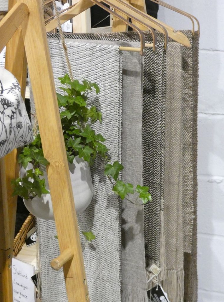 selection of woven scarves on a wooden stand with hanging plant