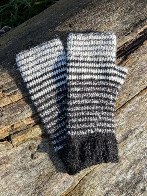 pair of black white and curlew striped wrist warmers laid on a log in the sunshine